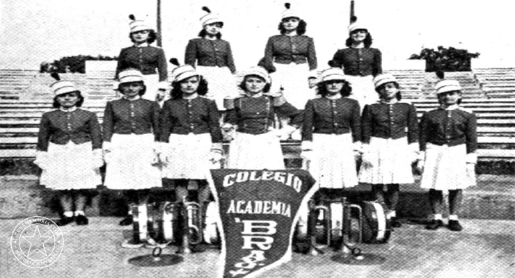 Integrantes uniformadas de la Banda de Música del Colegio y Academia Bravo, con instrumentos de percusión y el estandarte del establecimiento.